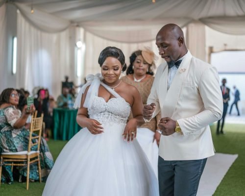 A joyful African bride and groom enjoying their wedding celebration indoors with guests.